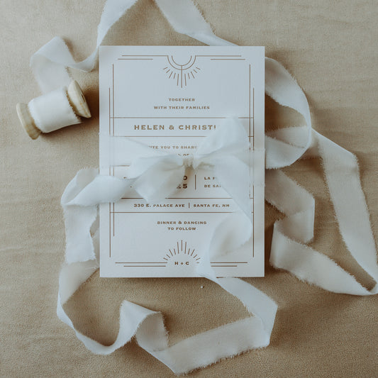 Raw edge, hand-dyed silk ribbon, shown wrapped around a wedding invitation in a styled flat lay, highlighting its handmade quality