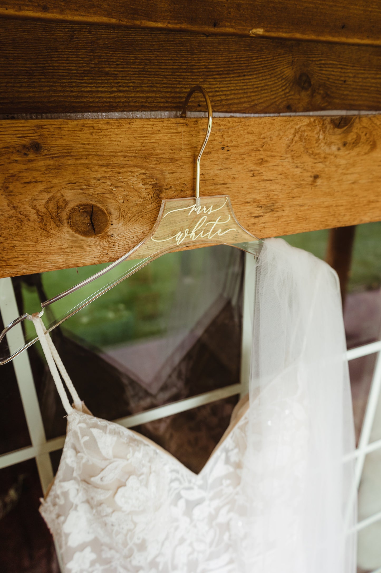 A clear acrylic hanger featuring the name 'mrs white' in a gold script font, hanging a white wedding dress.